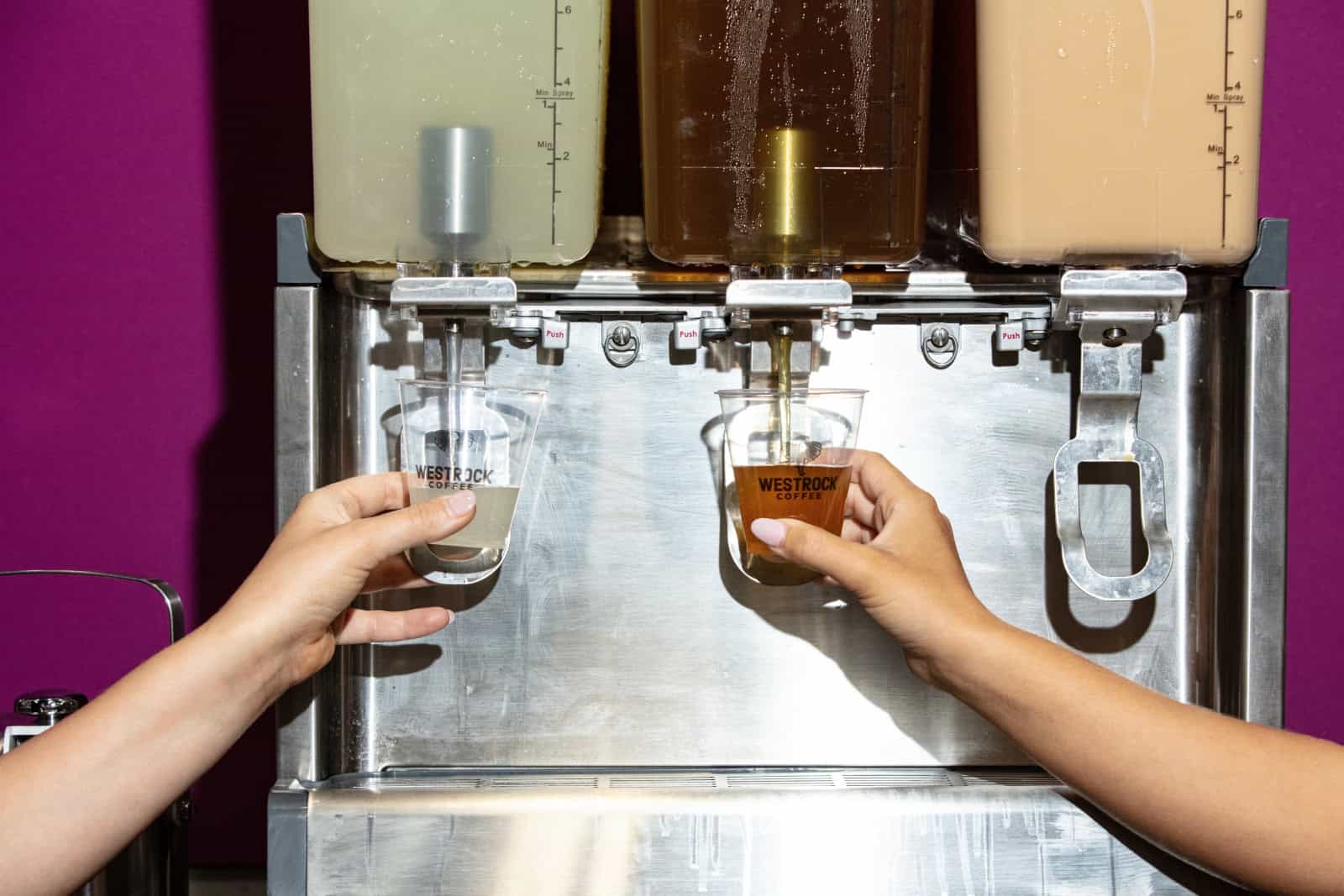 Hands holding cups under a beverage dispenser.